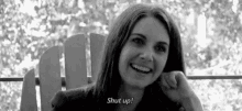 a woman is sitting in a chair and smiling with the words `` shut up '' written on her face .