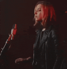 a woman in a leather jacket is singing into a microphone while playing a piano .