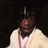 a man with dreadlocks is wearing a white sweatshirt and a gold chain around his neck