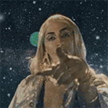 a woman in a white coat is pointing at the camera with a planet in the background .