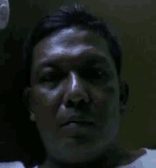 a man 's face is shown in a dark room with a white shirt on