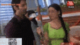 a man is holding a microphone and talking to a woman in a green top