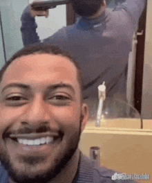 a man with a beard is taking a selfie with a gun in his hand in front of a mirror .