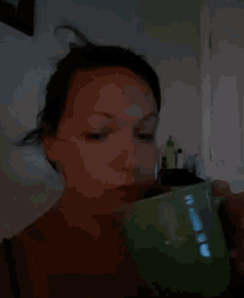 a woman is drinking from a green cup with her eyes closed
