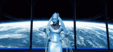 a woman in a silver dress is standing in front of a window looking out to the earth