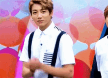 a young man wearing suspenders and a white shirt is standing in front of a wall of balloons .