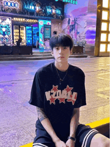 a young man wearing a black t-shirt that says kz041 sits on the sidewalk