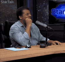 a man sits at a table with a microphone in front of a sign that says star talk