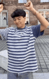 a man wearing a blue and white striped shirt is dancing with his arms in the air