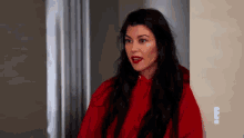 a woman with long black hair and red lipstick is standing in a room .