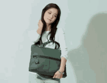 a woman in a white shirt is holding a gray purse