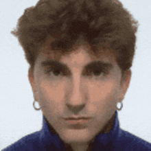 a close up of a man 's face with a blue shirt and earrings