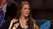 a woman is sitting on a couch wearing a jacket and a necklace and making a funny face .