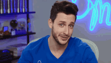 a man in a blue shirt is sitting in front of a neon sign