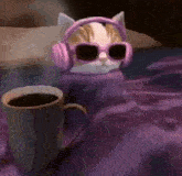 a cat wearing headphones and sunglasses is sitting next to a cup of coffee on a bed .