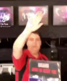 a woman in a red shirt is raising her hand in the air while standing in front of a counter .