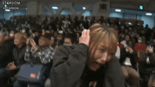 a man in a black hoodie is covering his face with his hands in a crowd .
