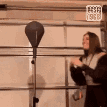 a woman is standing in front of a punching bag with the year 1968 on it .