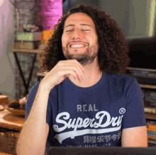 a man with curly hair is wearing a blue superdry t-shirt