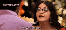 a woman wearing glasses is talking to a man and saying `` they 're samosas ! ''