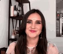a woman with long dark hair is standing in front of a bookshelf and smiling .