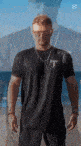 a man wearing sunglasses and a black t-shirt is standing in front of a blue background .