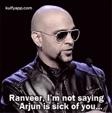 a bald man wearing sunglasses and a leather jacket is talking into two microphones .