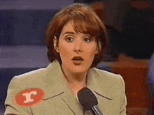 a woman wearing a badge with the letter r on it stands in front of a microphone