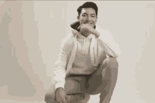a man in a white hoodie is squatting down and covering his face .