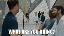 a group of men are standing in front of a climbing wall with the words what are you doing