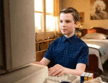 a young boy in a blue shirt is using a computer in a bedroom .