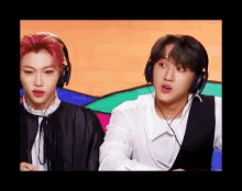 two young men wearing headphones are sitting next to each other on a stage .