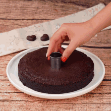 a person cutting a hole in a chocolate cake on a plate