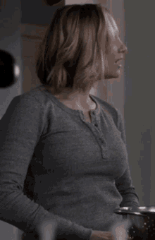 a woman in a grey shirt is standing in front of a pot