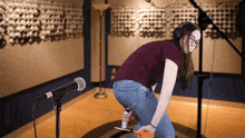a woman wearing headphones is kneeling in front of a microphone and holding a can of elmer 's glue