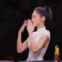 a woman in a white dress is sitting at a table with her hands folded .