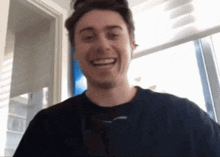 a man is smiling in front of a window