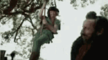 a man with a beard is standing next to a tree with a person hanging from it .