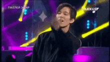 a man in a black shirt is dancing on a stage in front of a purple and yellow light .