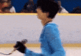 a man in a blue jacket is holding a pair of ice skates on a rink .