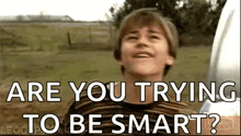 a young boy is standing in a field with the words `` are you trying to be smart ? '' written on the screen .