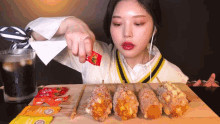 a woman is pouring ketchup on a hot dog on a stick