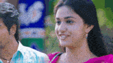 a man and a woman are standing next to each other and the woman is wearing a pink saree .