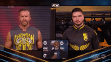 two men standing next to each other in front of a screen that says aew