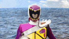 a purple ranger with a heart shaped helmet stands in front of a body of water