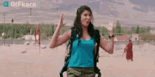 a woman with a backpack is waving her hand while standing in the desert .