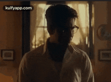 a man in a white shirt and glasses is standing in front of a window in a dark room .