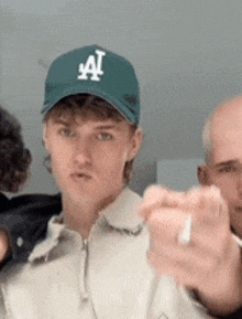 a young man wearing a la hat is pointing at the camera .