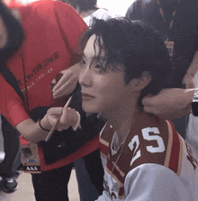 a man wearing a number 25 shirt is getting his hair done