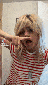 a girl in a red and white striped shirt is making a funny face with her finger in her mouth